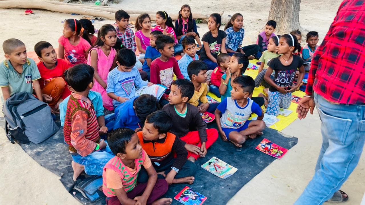 A volunteer leads an outdoor community learning session with a large group of children